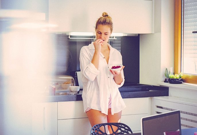 image of woman eating berries at a kitchen counter