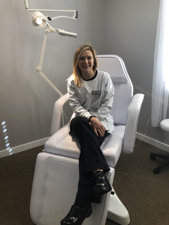 smiling woman in white coat seated in patient chair in medical aesthetician office