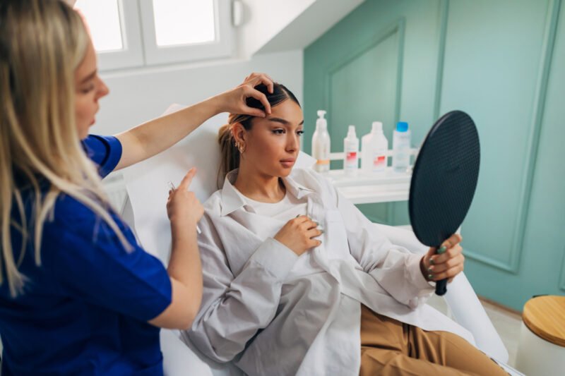 Young Woman Looking in Mirror After Injectables Performed by a Highly Qualified Certified Injector