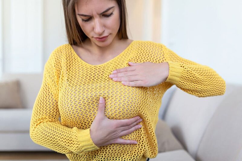 Frowning woman places hands around left breast to check breast implants