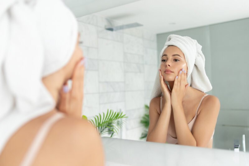 Young woman looks at skin in mirror using skincare to treat melasma