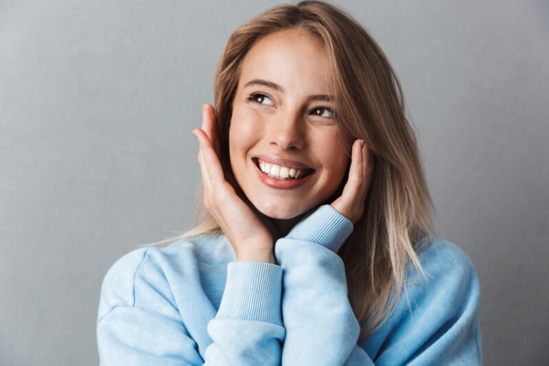 Young woman wearing winter sweater smiling and touching face after non-surgical skin treatments at Hagerstown med spa